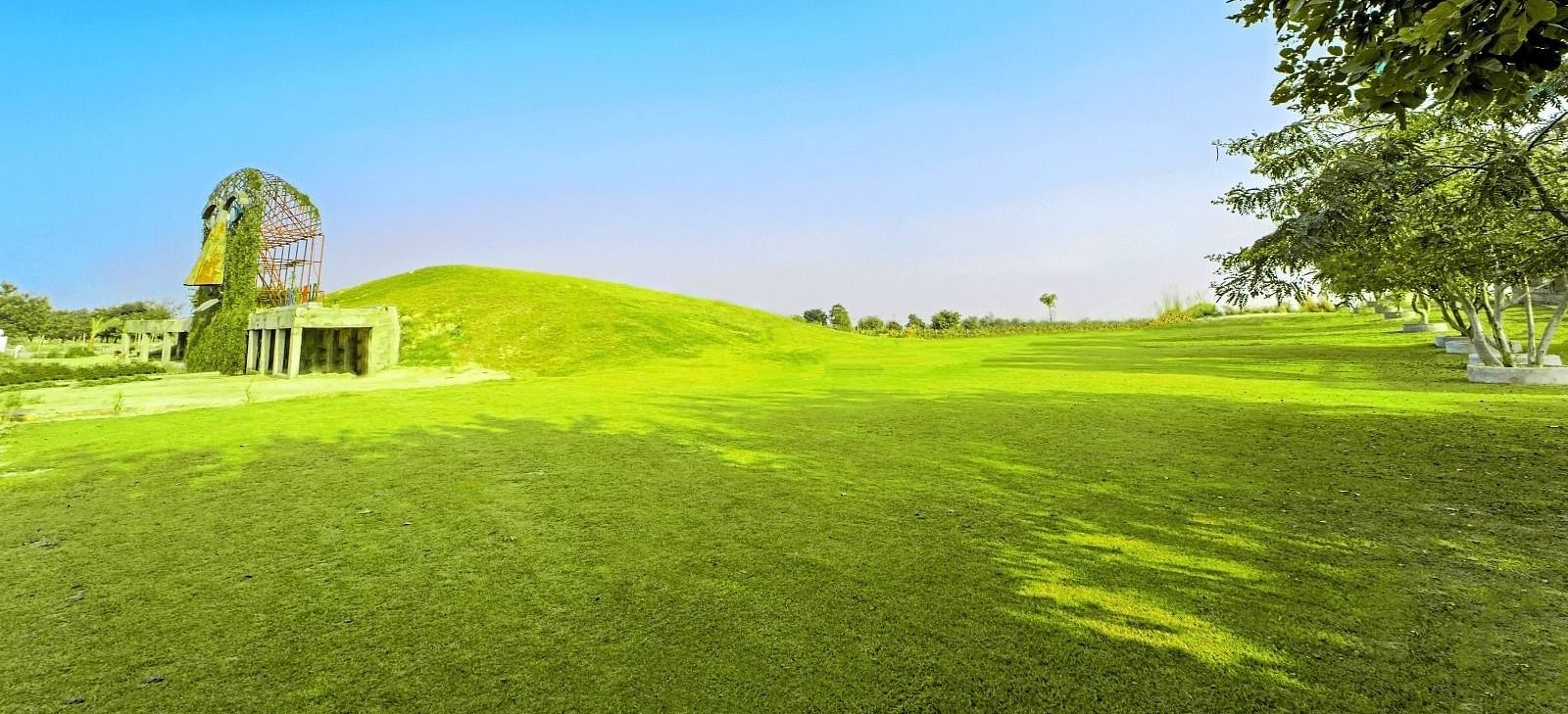 Vast lawn with the artistic mask sculpture of Grassfield Riveria Resort, Jaipur, set against a clear sky.