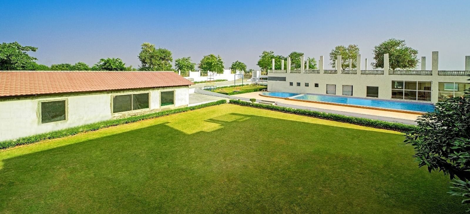 Expansive lawn with a swimming pool and buildings in the background at Grassfield Riveria Resort, Jaipur.