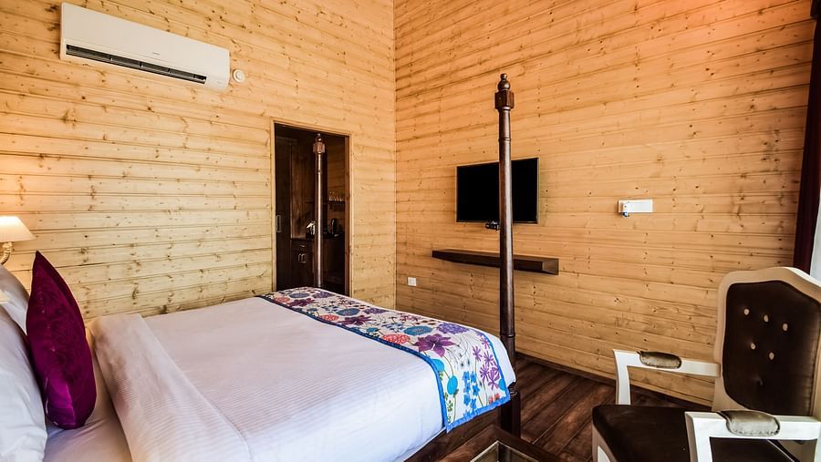 A cosy room with wood-paneled walls, a bed, a mounted TV, and an air conditioner.- Bamboo Saa Resort & Spa, Udaipur
