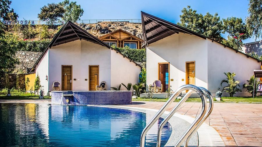 Two modern bungalows with pointed roofs flank a swimming pool.