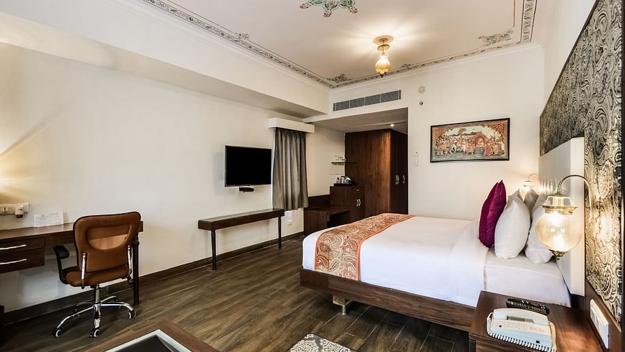  A hotel room with a large bed, a desk, and a seating area with warm lighting.- Bamboo Saa Resort & Spa, Udaipur