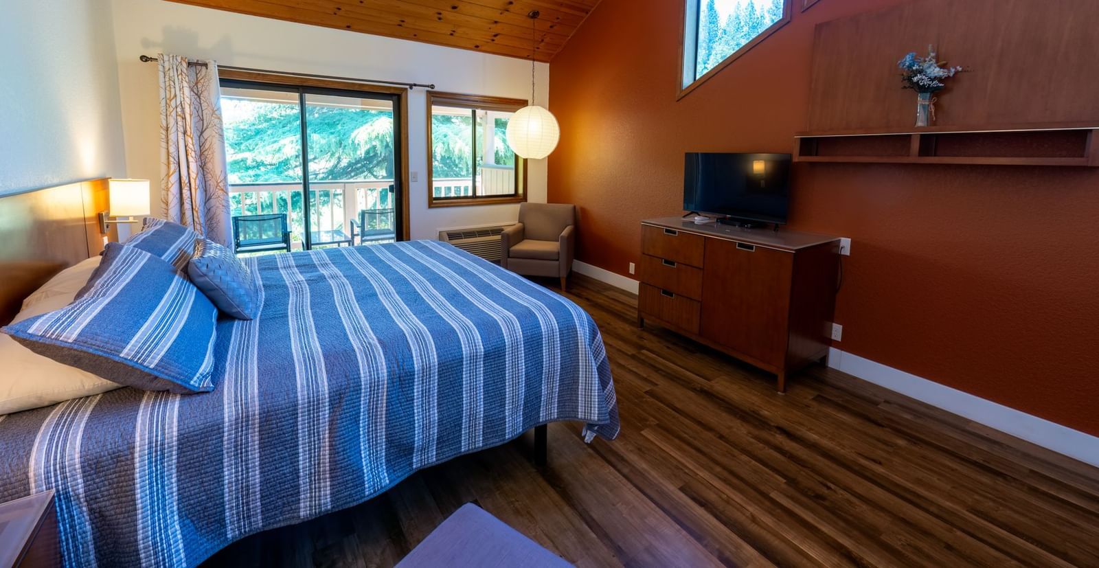 A Deluxe King Room at Amador Hotel with a wooden ceiling, a king-sized bed with striped bedding, and a TV on a dresser.