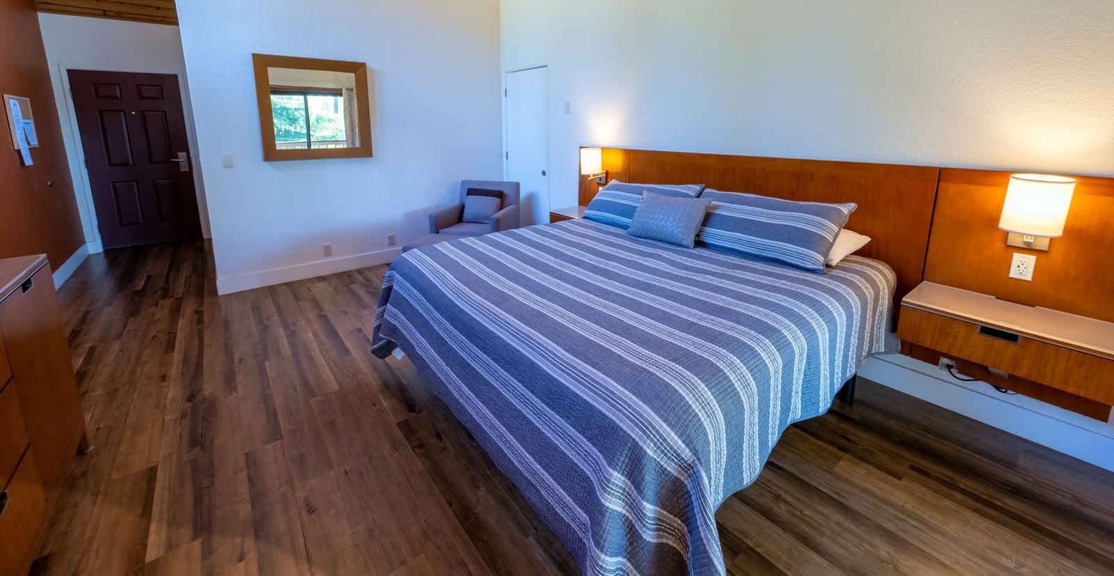Deluxe King Room at Amador Hotel with a king-sized bed, wooden flooring, wall lamps, and a mirror above a dresser.