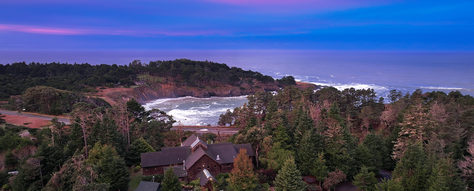 Stunning aerial view of the coastline at sunset, with a vibrant purple and pink sky over the ocean - Brewery Gulch Inn & Spa