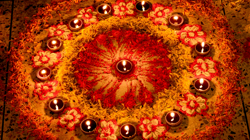 A close up view of a rangoli made with rose petals and lit diyas in a circle during a Diwali party in Mumbai.