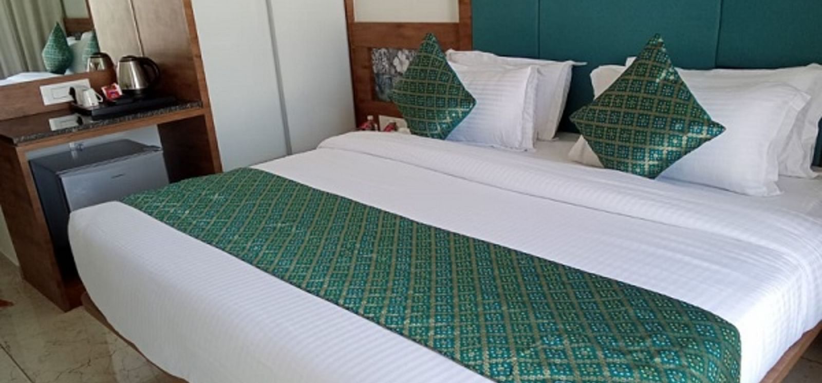 A room with a large bed which is neatly made with bedsheet, pillows and bedside tables at Angel Lords Eco Inn Amreli.