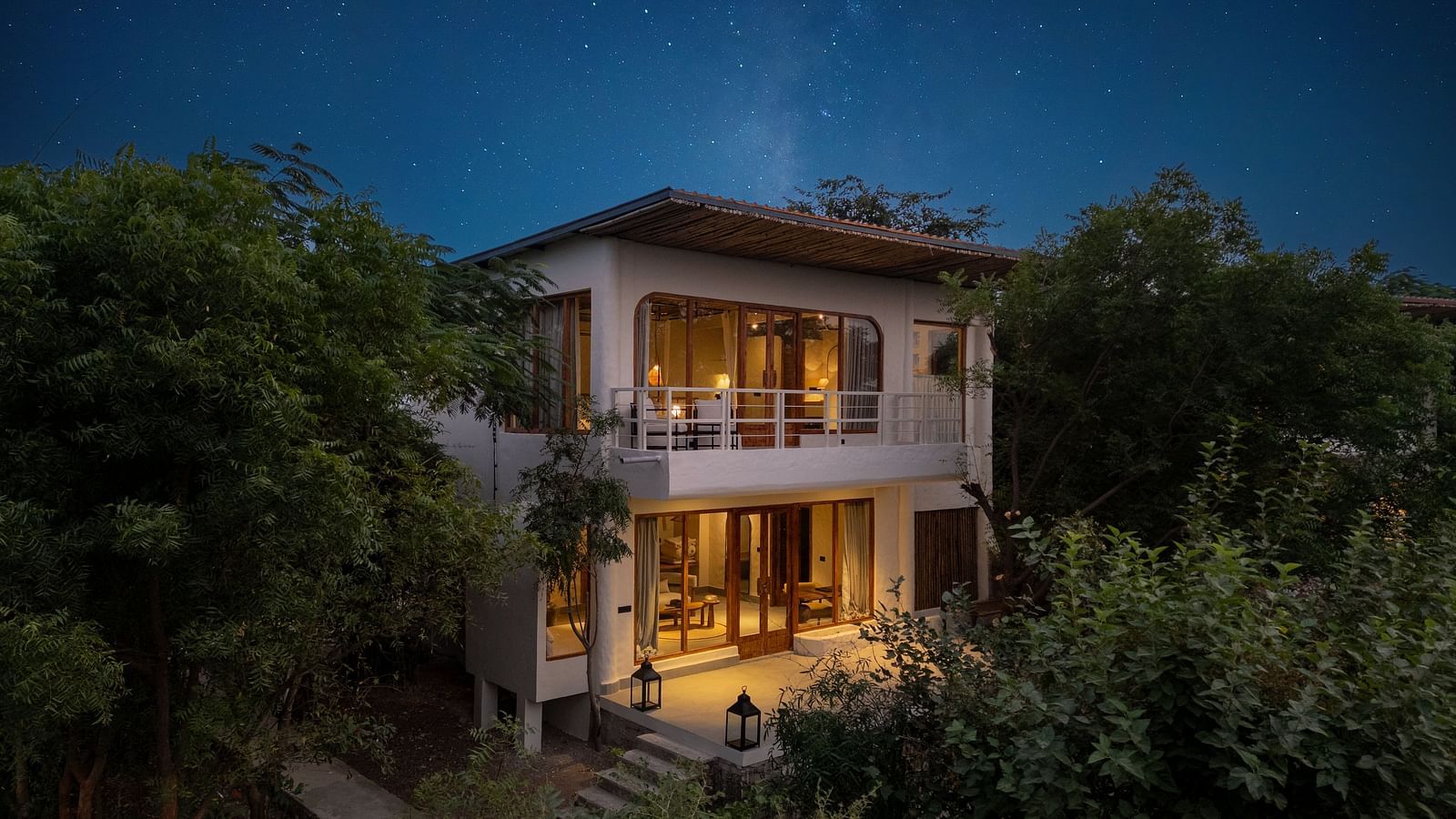 Exterior of a modern two-story villa surrounded by trees and plants.
