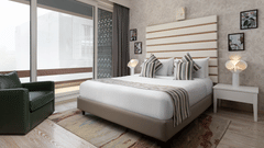 A stylish room at The Atara, Gurugram boasts a comfortable bed with a patterned runner, a plush green armchair, and a large window that offers a scenic outdoor view