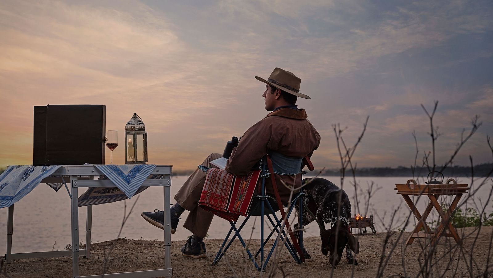 image of a man relaxing and enjoying the mesmerising sunset with a serene lake in front of him at dev shree deogarh