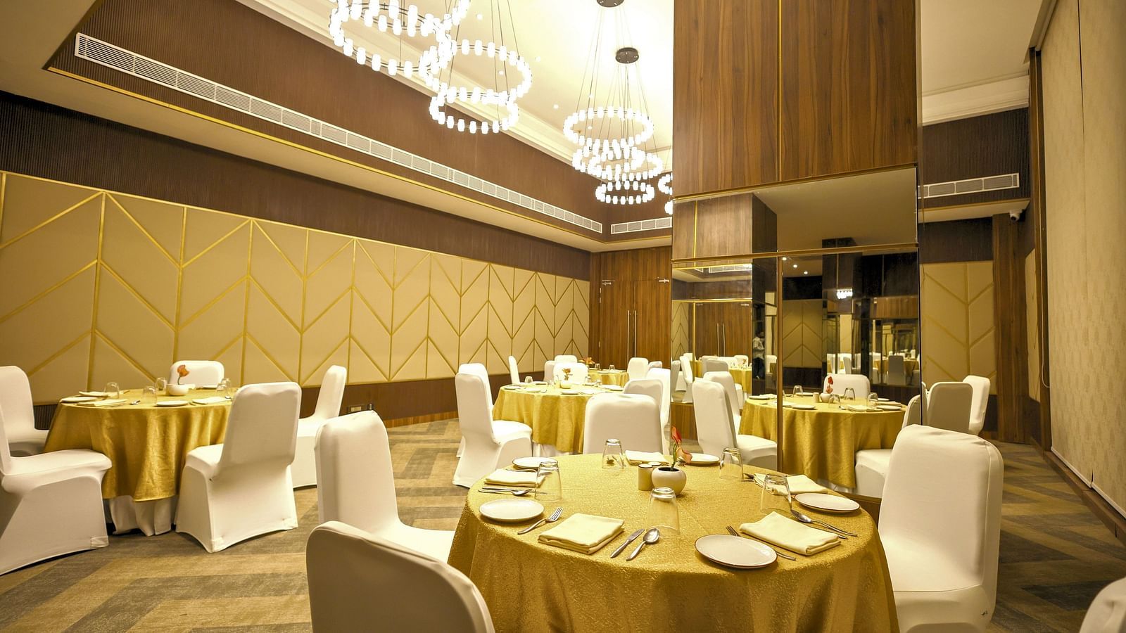 A banquet hall set up with round tables draped in brown linens and white chair covers, ready for a special event at Rhythm Gurugram Hotel and Suites. 