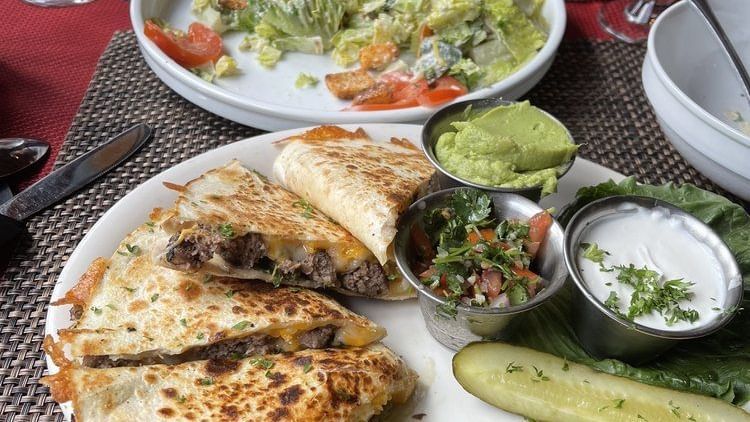 A table setting featuring a meal with a quesadilla, guacamole, salsa, and a side salad