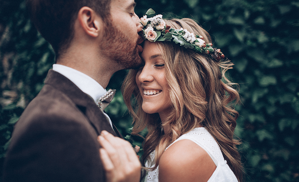 a happy couple dressed in wedding attire with the groom kissing the brides forehead