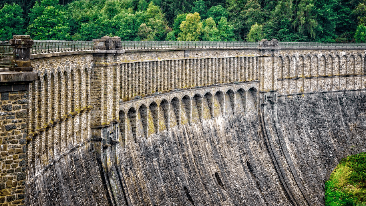 an image of a dam wall with gaps in between with lush green trees in the background