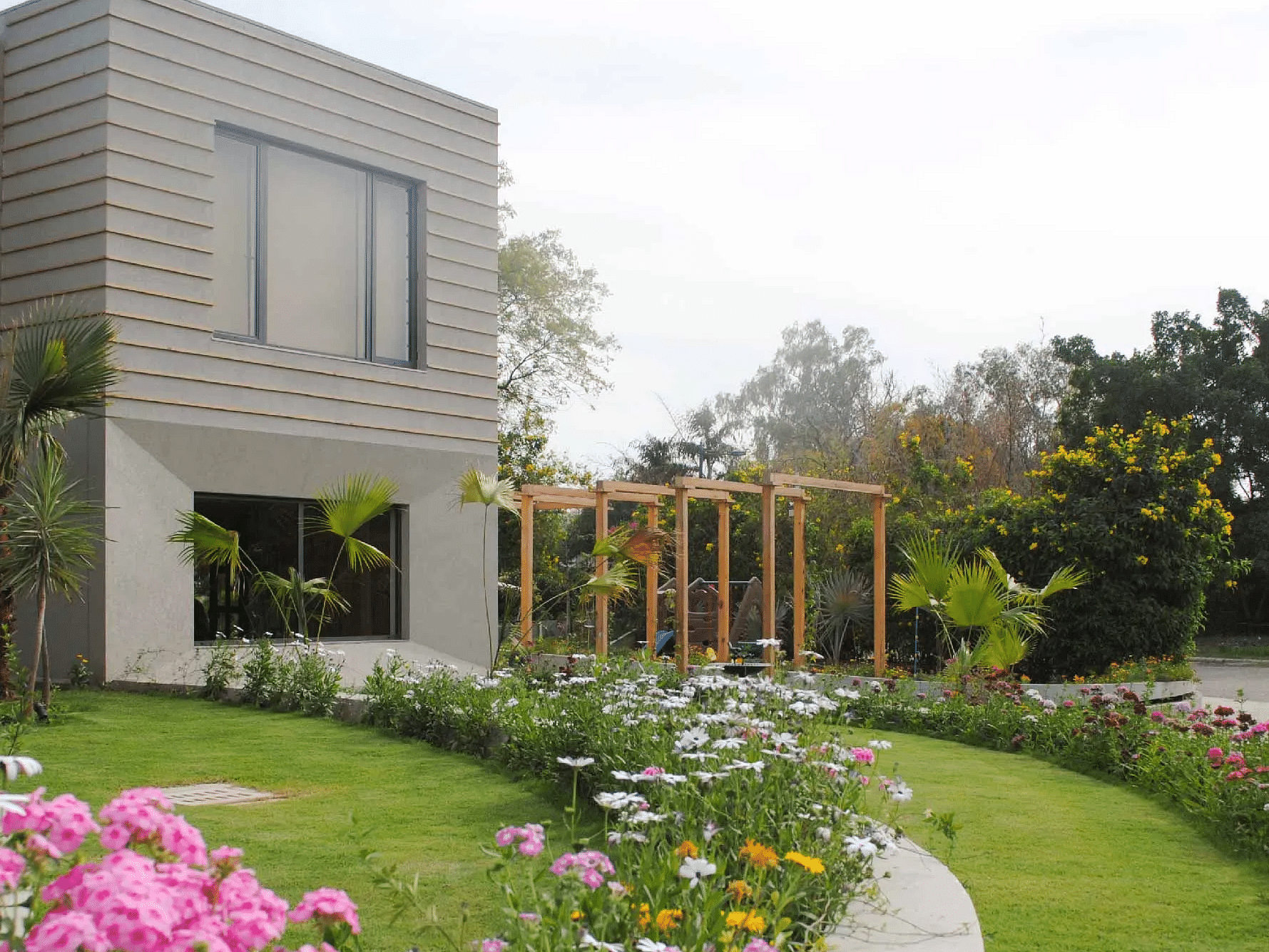 Modern house with a curved garden path bordered by pink and white flowers, and a green lawn at Karma Chalets. 