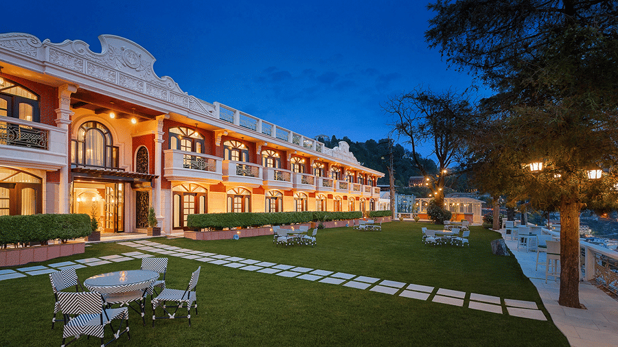 Outdoor tables and chairs, on a green lawn in front of a lighted building at night at Ramada by Wyndham Mussoorie Mall Road.