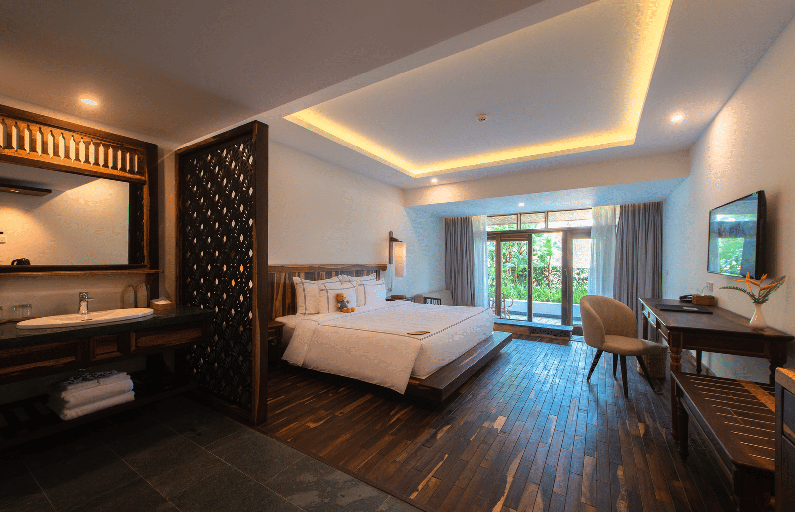 Balcony Room at Alibu Resort Nha Trang, Vietnam with a bed, tiled floor, wardrobe, side tables, open area to balcony and glass doors with view to outside trees.
