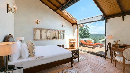 Corner view of the bedroom of a villa overlooking the outdoor balcony with 2 sun loungers basking in the sun - Golden Tulip Goa Mandrem