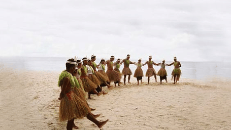 Group of people walking together on a sandy beach wearing traditional attire.