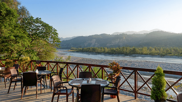 Outdoor dining patio with tables and chairs overlooking a river and mountains.