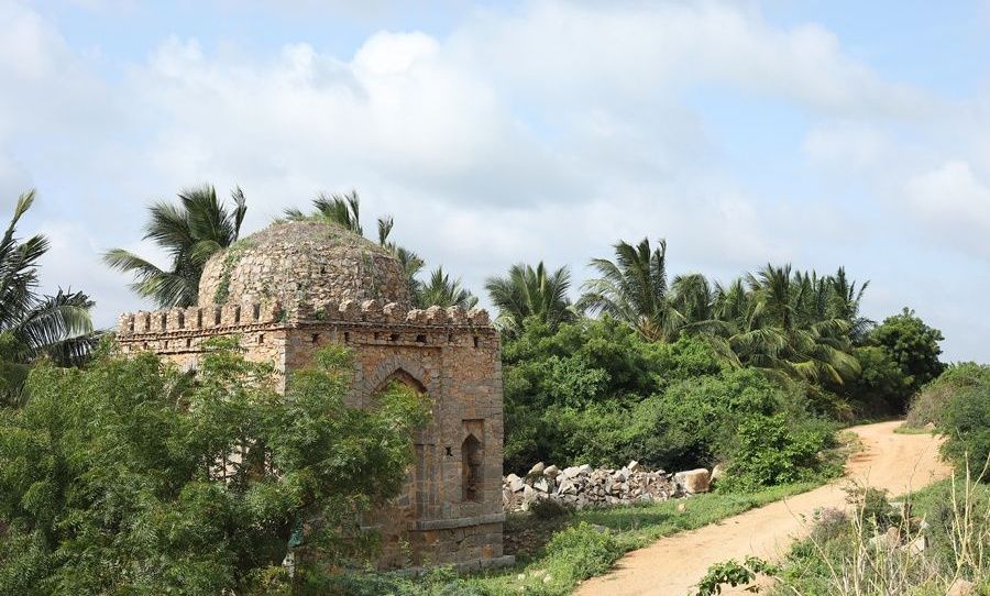 Stone dome structure amidst green trees and a dirt path.