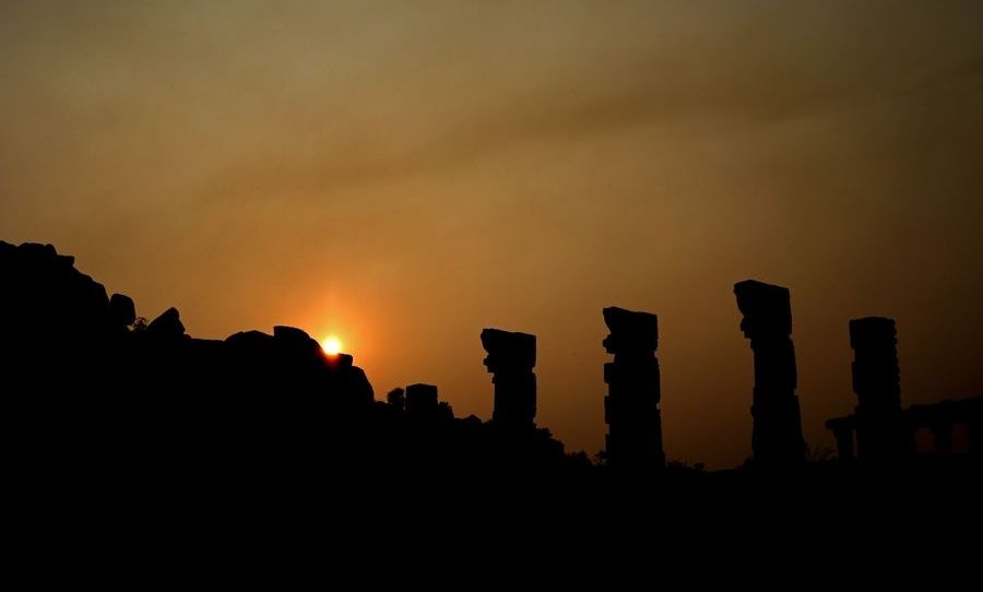 Silhouetted Hampi temple ruins at sunset.
