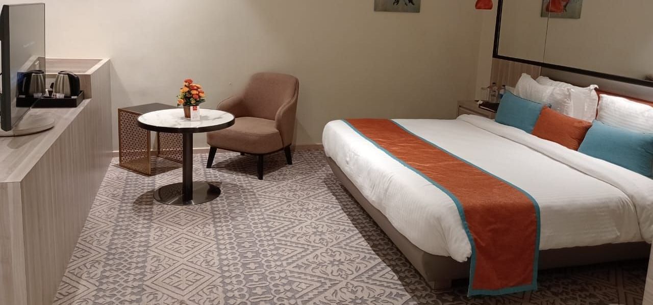 Modern hotel room with twin beds, a small table and chair, soft lighting, and minimalist decor.