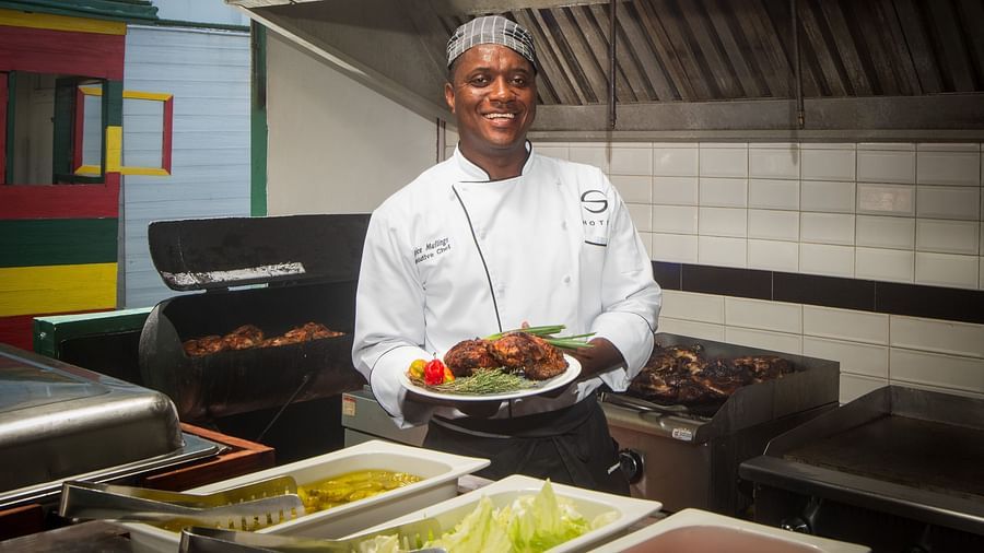 A chef holding a plate of grilled food in a kitchen  - S Hotel Montego Bay, Jamaica