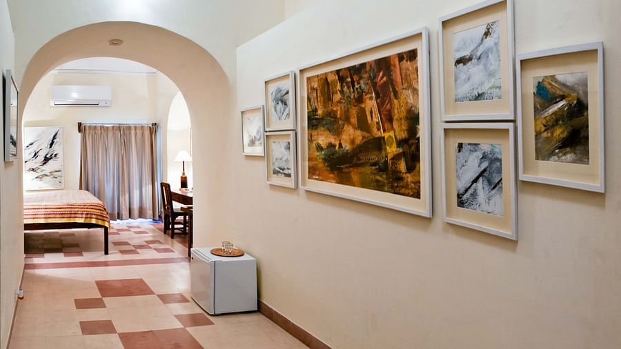 A hallway with an arched doorway leading to a bedroom, patterned floor tiles, and a collection of framed artwork on the wall, showcasing the fort-palace's artistic decor - Tijara Fort-Palace - 19th Century, Alwar.