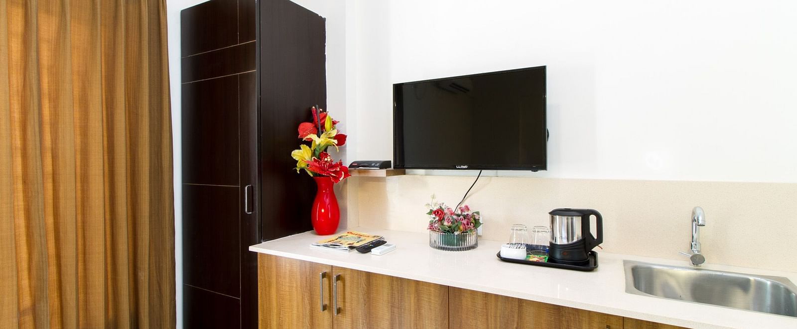 A room with a television, a small kitchen area, and a wardrobe at Sanctum Suites Whitefield, Bangalore.