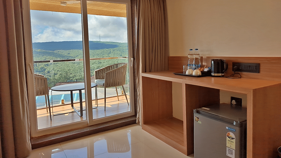 Room with a work desk, minibar, wooden furnishings, and balcony overlooking green hills