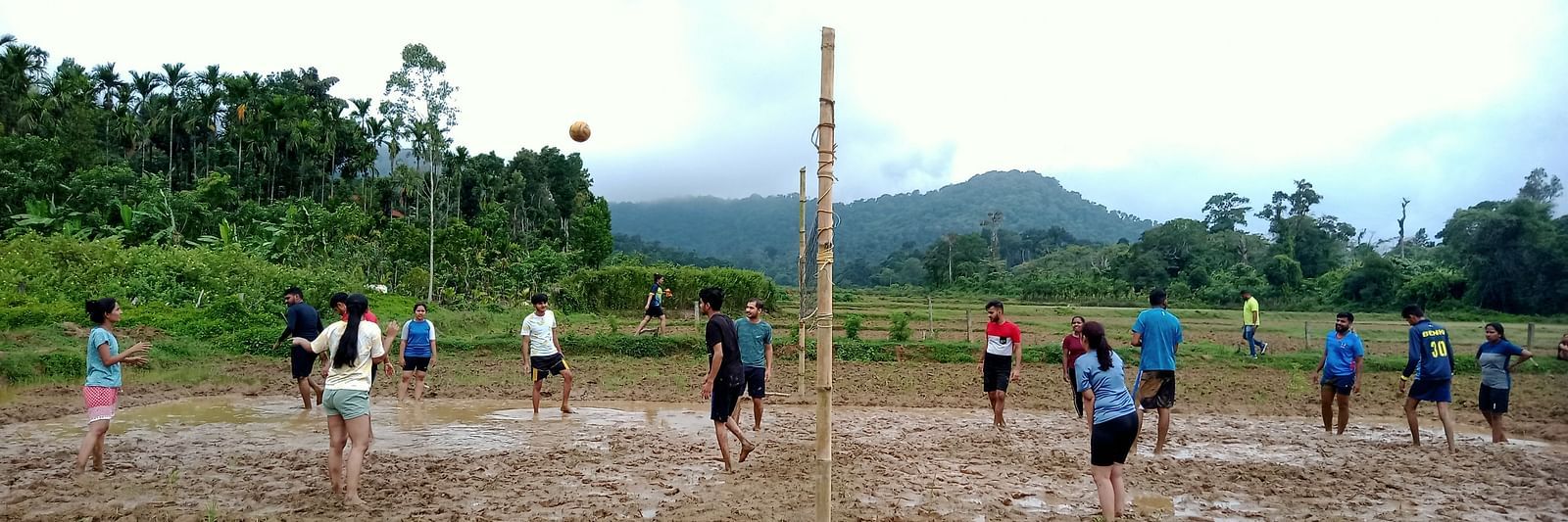Group playing volleyball in a muddy field with a scenic mountain backdrop - Evergreen County