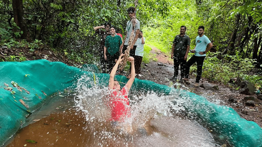 Adventure participant splashing into a water obstacle during a guided forest activity.