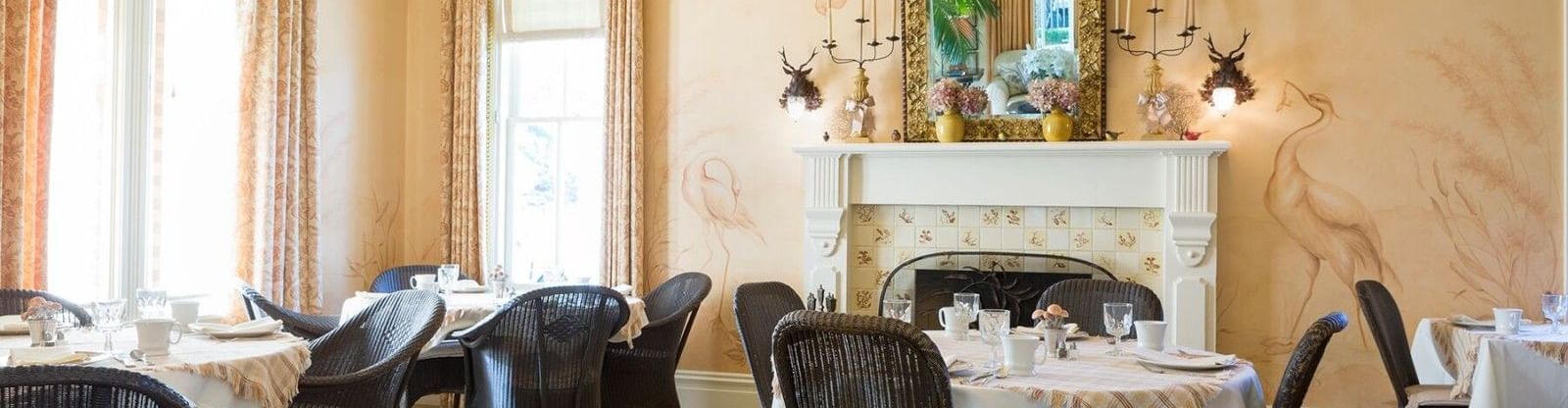 The elegant dining room at the Tallman Hotel features a fireplace, mirrors, and set tables with natural light.
