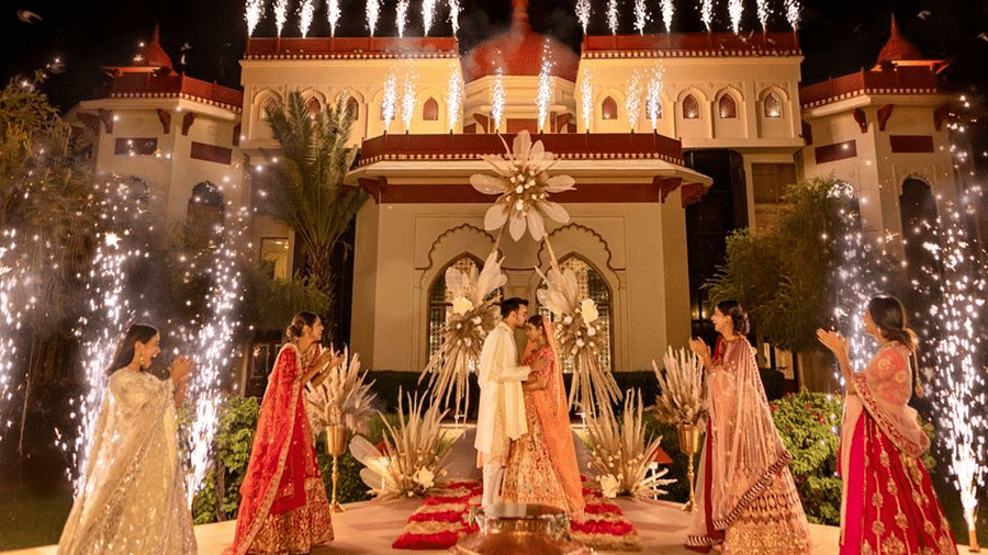 A couple standing under a floral archway at The Ummed Jodhpur, surrounded by friends and family holding sparklers, with the palace illuminated in the background.
