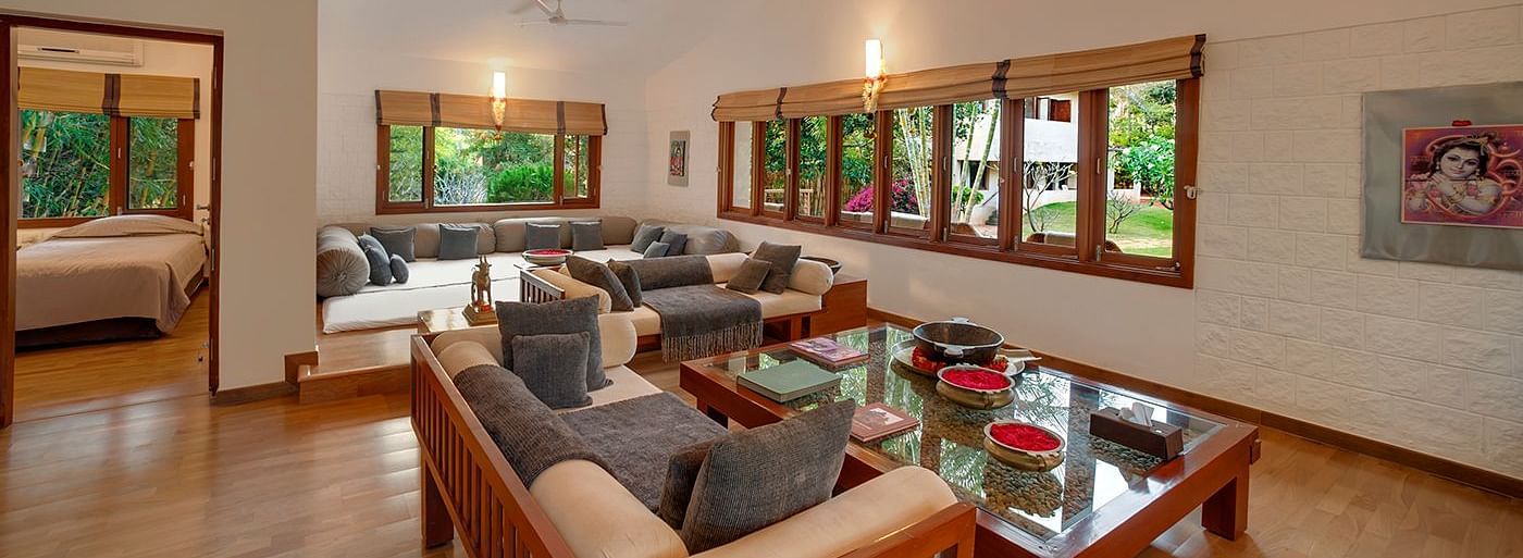 A living room with a couch, armchairs, a coffee table, and large windows - Shreyas Retreat