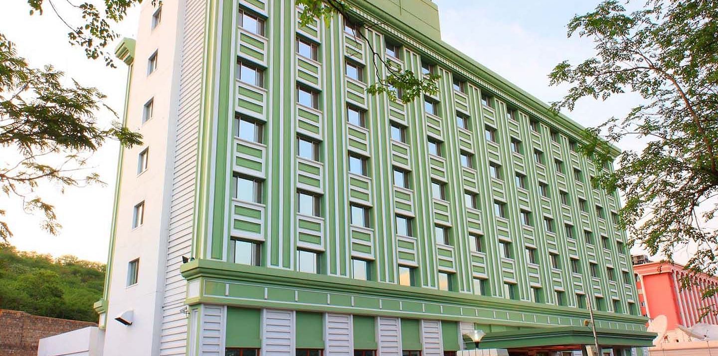 A multi-story green hotel building flanked by trees at Tara, Comfort Hotel in Hyderabad - Ramoji Film City.