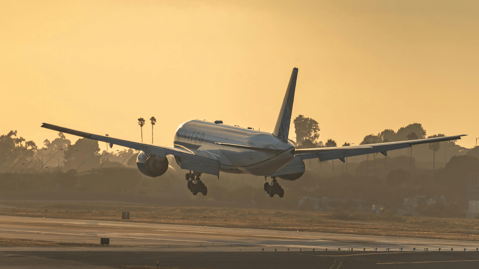 Airplane taking off or landing on runway during sunset, with sky glowing in the background.