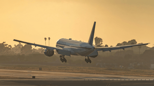 Airplane taking off or landing on runway during sunset, with sky glowing in the background.