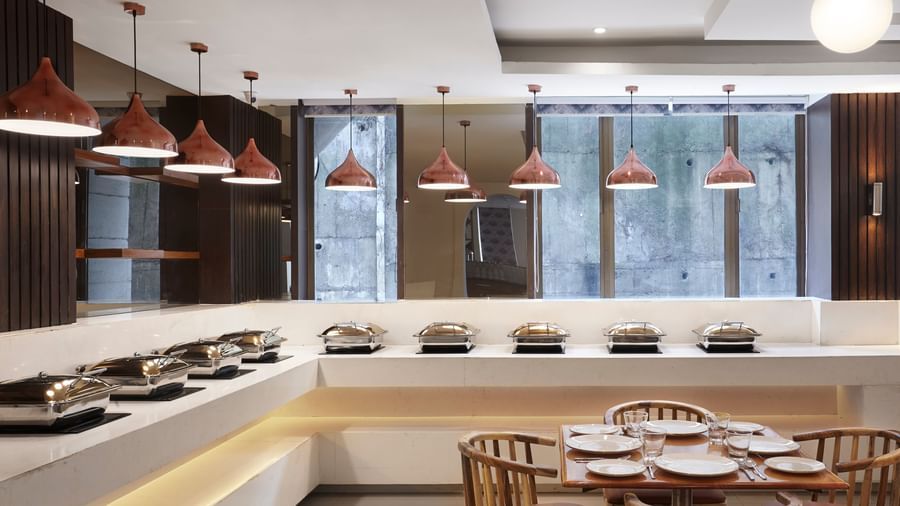 The open kitchen and dining area at Monday Hotels Mahape, Navi Mumbai, with a buffet-style counter and dining tables.