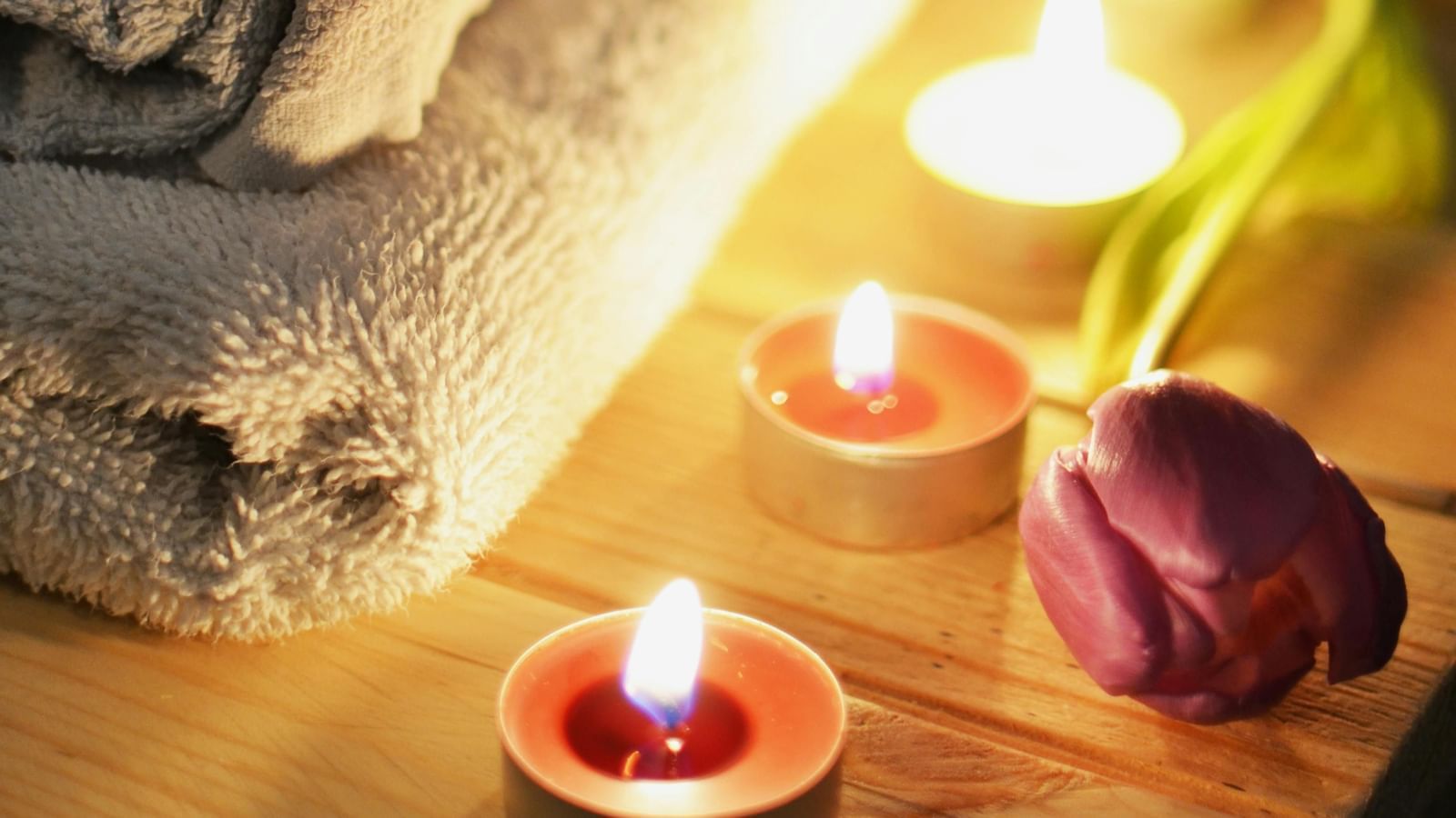 Spa setting with towels, candles, and shells on a wooden surface.