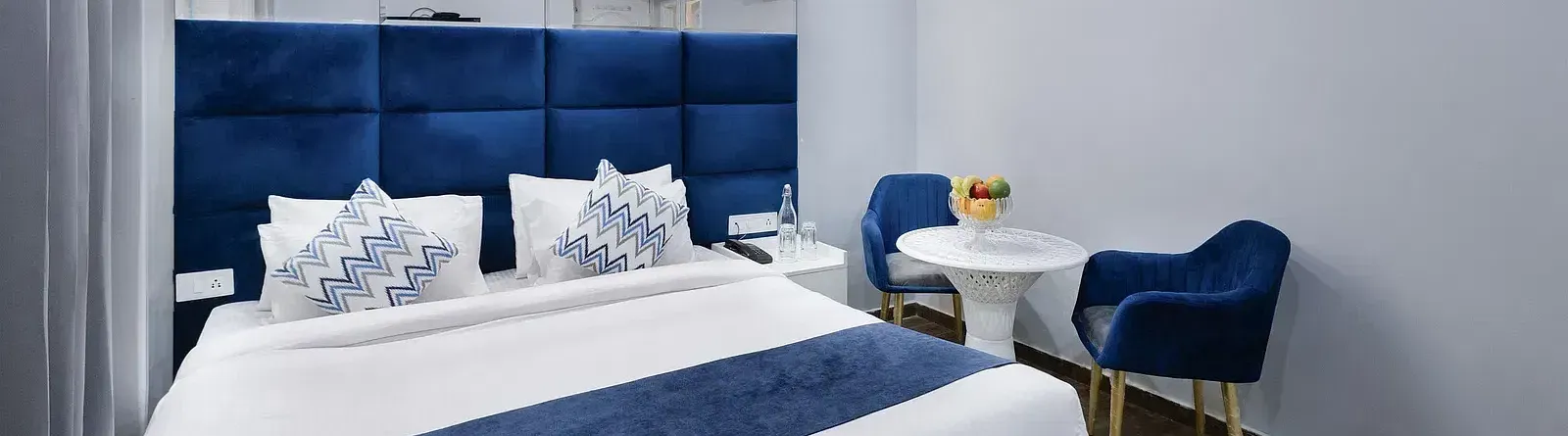 Deluxe Room featuring a king size bed with blue accents, a small table with two chairs, and minimalist decor. - Hotel Downtown17, Chandigarh