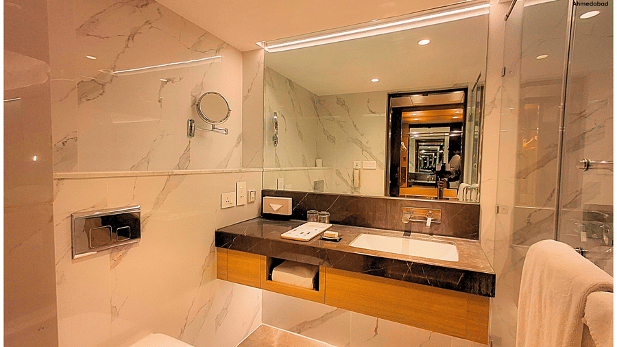 Deluxe King Room at Pride Plaza Ahmedabad featuring a spacious marble bathroom with wide vanity counter, modern fixtures, illuminated mirror and neatly arranged bath amenities.