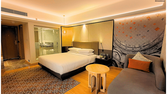 Superior King Room at Pride Plaza Ahmedabad displaying a spacious king size bed, contemporary wall art, plush seating, wooden flooring and soft ambient lighting for a refined stay.