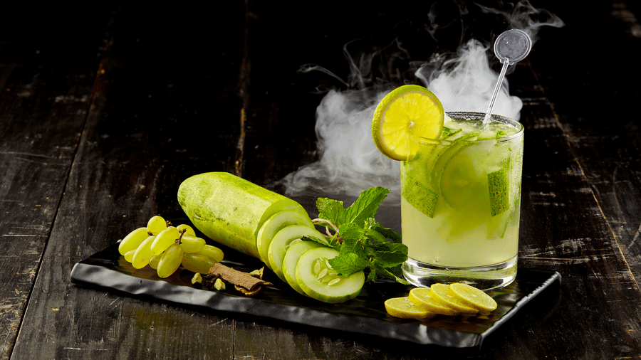 A smoky drink with lime wheel, cucumber slices, grapes, and mint on a slate board at The Citrine, Bangalore