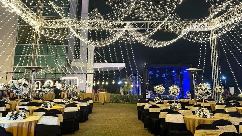  An outdoor nighttime event at Amer Greens with rows of tables set up on grass, all underneath a canopy of draped string lights, with a stage area visible in the distance.