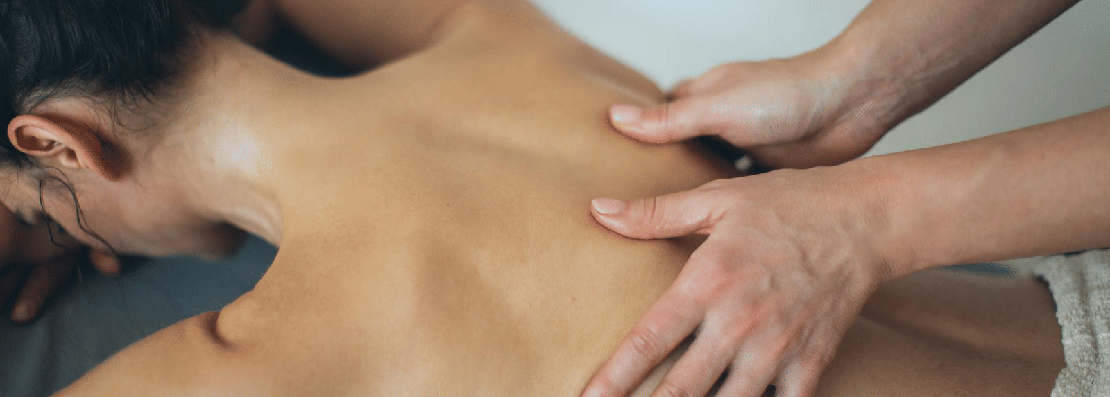 A lady laying faced down on a spa table receiving a back massage with oil