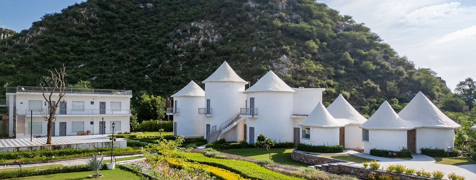 Conical-roof accommodations with an open space in front, set against a scenic mountain backdrop at Valley by Grassfield.