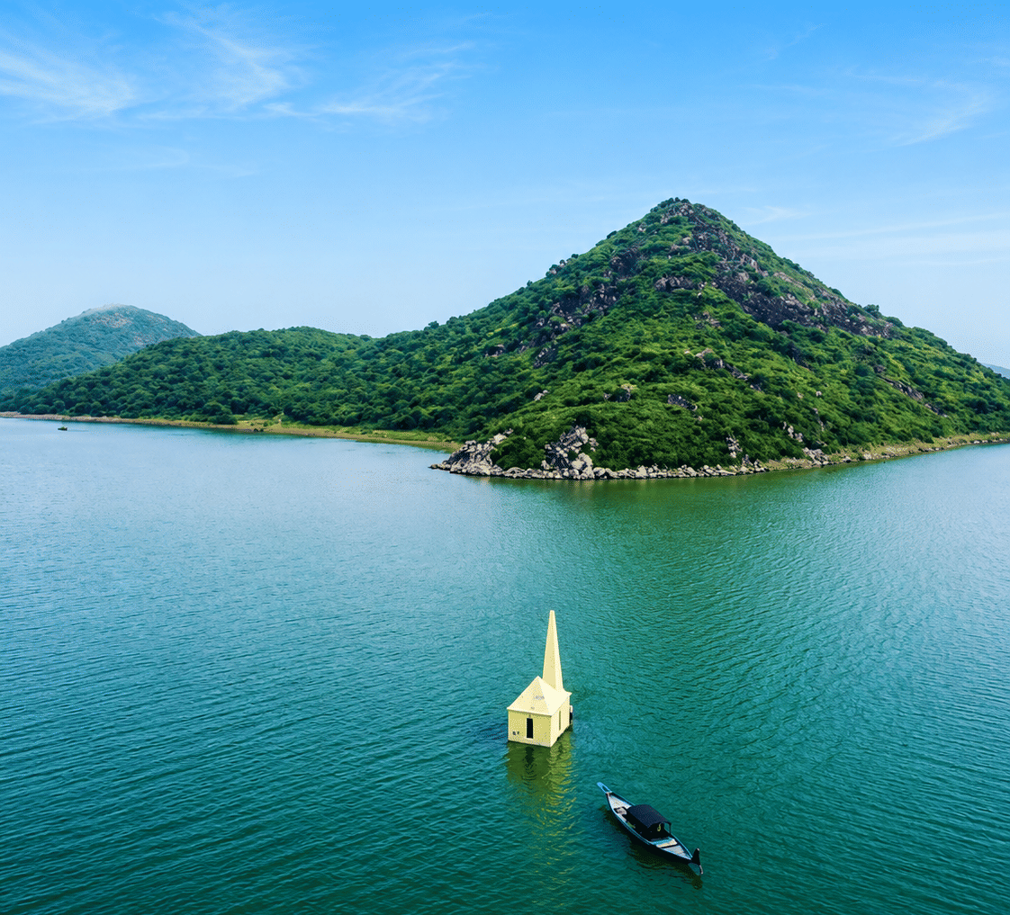 Chilika Lake with a forested island hill, a small yellow shrine standing in the water and a boat, near MAYFAIR Palm Beach Resort, Gopalpur-on-Sea.
