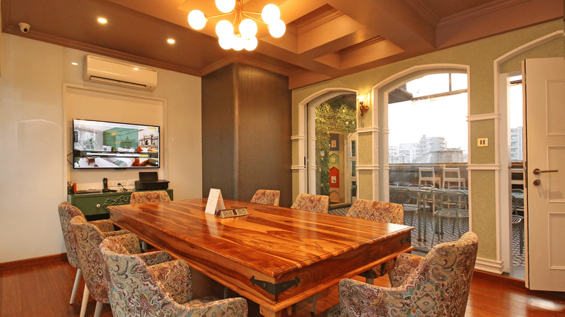Warm, stylish dining and meeting space at Theory9 Premium Service Apartments, Bandra, featuring a long wooden table, patterned chairs, soft lighting, and large windows with city views.