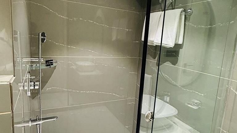 A shower enclosure with a glass door, a geyser, a towel and shower taps - Five Elements Hotels Goldleaf, Haldwani